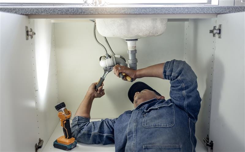 Plumber repairing pipes beneath a bathroom sink in Davenport