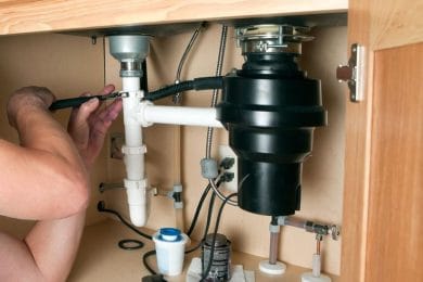 Plumber repairing a garbage disposal beneath a kitchen sink in Davenport