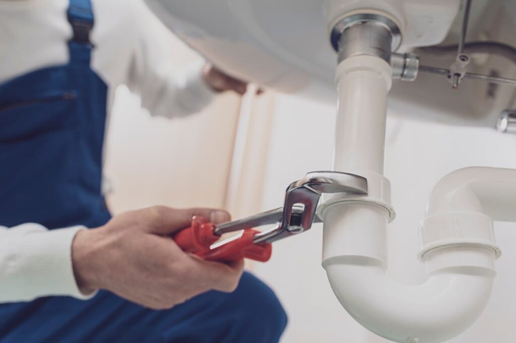 Plumber repairing a white drain pipe beneath a sink in Davenport
