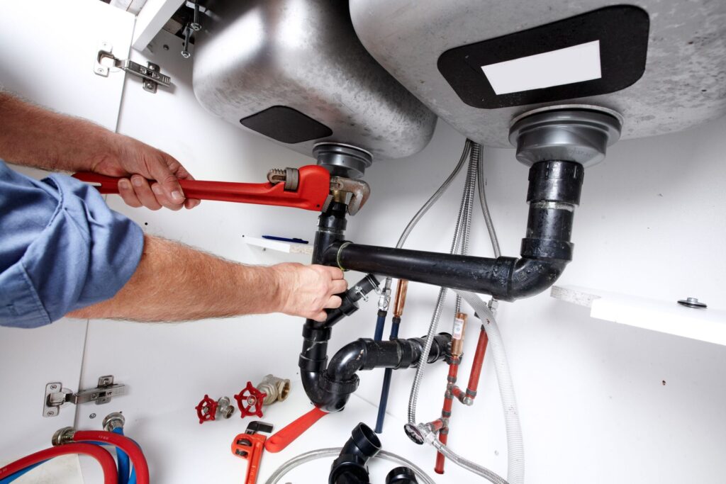 Plumber repairing drain pipes beneath a kitchen sink in Davenport